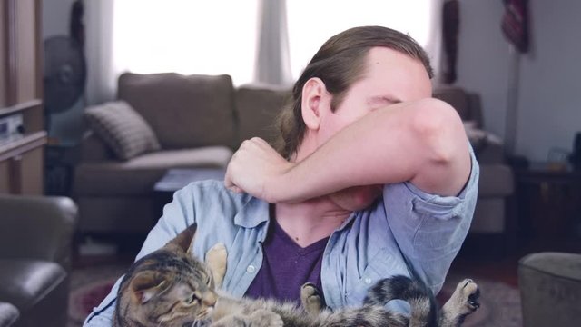 A caucasian man coughs into his elbow and cuddles a cat - slow motion