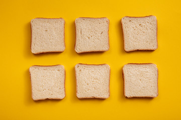 Top view of square pieces of bread. Six square of toast, white bread on a bright yellow background.