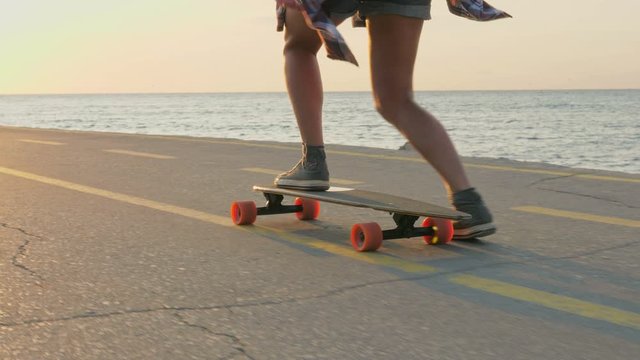 Young woman skating on a skateboard on a beach coastal alley at Sunrise. Girl riding long board, HDR 4K, Slow motion.