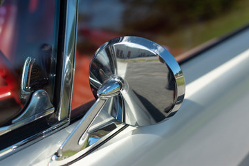 Chrome mirror of an old American muscle car. White classic car with red interior.