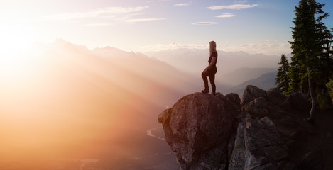 Fantasy Adventure Composite with a Girl on top of a Mountain Cliff with Dramatic Nature in Background during Sunset or Sunrise. Landscape from British Columbia, Canada. Panorama