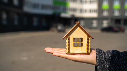 Obraz na płótnie Canvas Close up of small wooden house in woman's hand on background of built house. Concept of purchasing new apartment.
