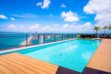 The beautiful blue swimming pool on the top roof of building with blue sea and blue cloudy sky background. 