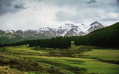 Analog slide photograph of a Mountain range over a dense forest and open meadow 