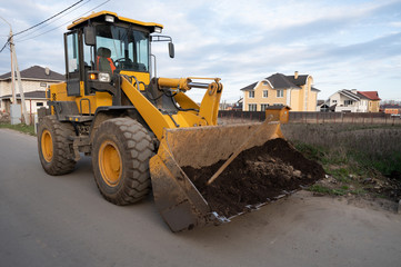 Yellow excavator bucket with black earth in scoop