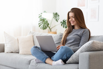 Happy young woman using laptop on couch at home