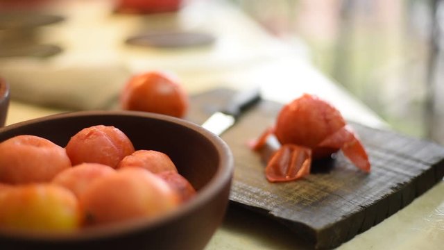 tomate pelado sobre tabla de madera con un cuchillo y cuenco con tomates pelados listos para su uso, en la cocina de una casa familiar
