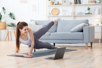 Sporty cheerful woman exercising at home, watching videos on laptop
