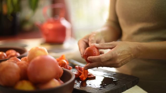 manos pelando tomates sobre tabla de madera en la cocina de un hogar familiar con un cuenco lleno de tomates ya pelados y listos para su proceso