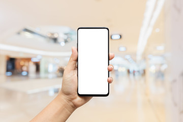 Mockup, person hand holding blank white screen mobile smart phone with blurred background of modern luxury department store for your advertisement artwork