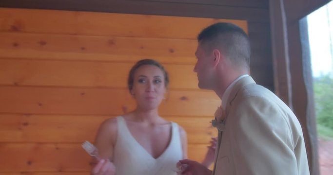 A bride and groom feed each other wedding cake while cameras flash at their mountain cabin reception. The groom kisses the bride and she bounces giddily.