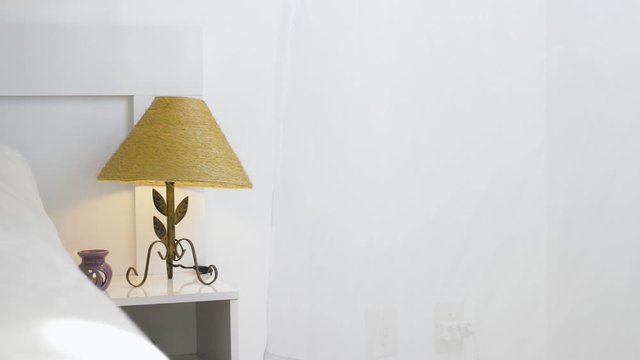 Lampshade on a bedside table with the curtain moving because of the wind.