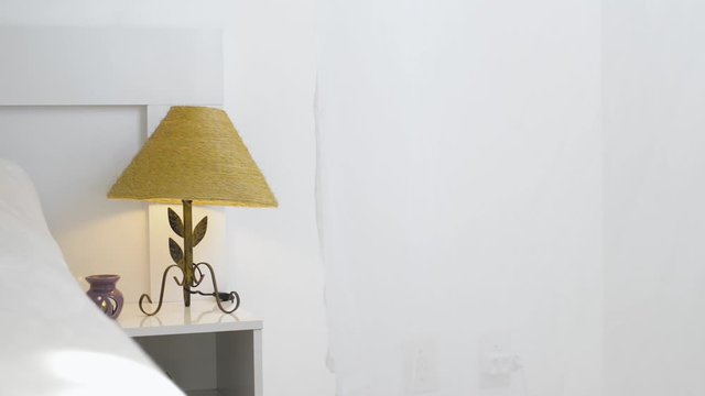 Bedside lamp on a bedside table with the curtain moving because of the wind. Stay at home concept.
