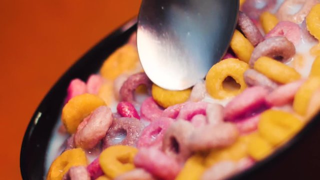 Colorful Cereals in a bowl with milk and a spoon in slowmotion.