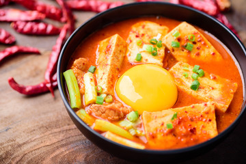 Kimchi soup with tofu and egg in a bowl on wooden background, Korean food (Kimchi Jjigae)