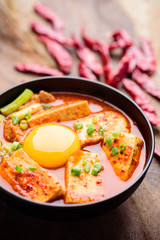 Kimchi soup with tofu and egg in a bowl on wooden background, Korean food (Kimchi Jjigae)