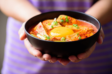Kimchi soup with tofu and egg in a bowl holding by hand, Korean food (Kimchi Jjigae)