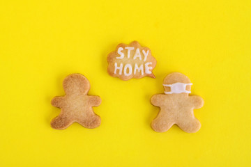 Homemade shortbread cookies with white glaze on yellow background, top view. Two men one of them in face mask and with callout cloud with text ‘Stay home’.
