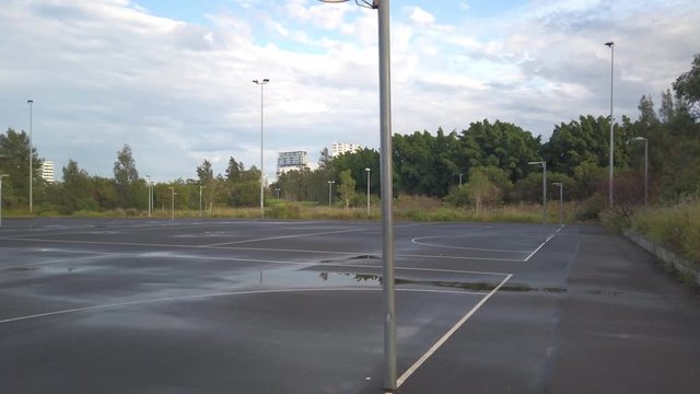 Empty wet netball field in a public park. Slow tilting up.