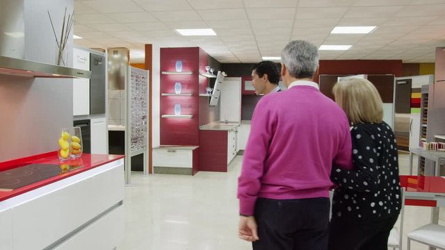 WS DS TS Salesman showing kitchen showroom to mature couple