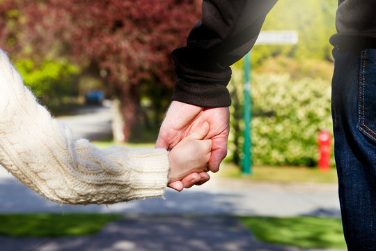 Small child holds her father's hand to cross the street safely;  Young daughter holds dad's hand as he takes her to school