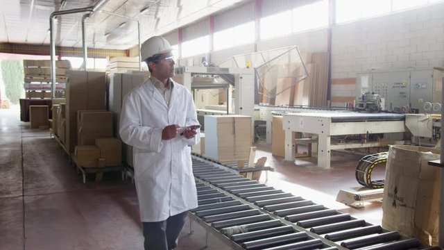 WS DS TS Man in lab coat and hardhat walking along furniture production line
