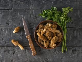 A knife and parsley leaves next to a bowl of morels.