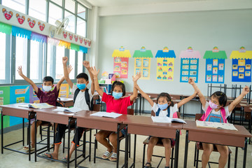 School kids wearing protective mask to Protect Against Covid-19,Group of school kids with teacher sitting in classroom and raising hands,Elementary school,Learning and people concept.