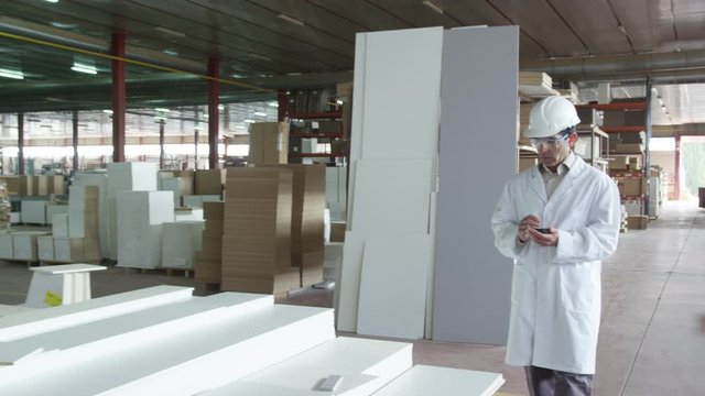 WS&nbsp;DS&nbsp;TS Man in lab coat and hardhat walking in furniture factory warehouse