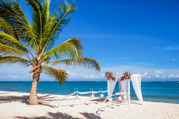 Colorful wedding arch gazebo pavilion made of bamboo and textile with fresh flowers decoration at sandy beach on sunny day for destination wedding ceremony in Dominican republic  