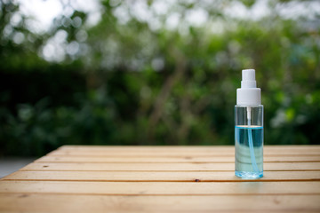 Blue alcohol can prevent Covid 19 placed on a wooden table on a green tree background.