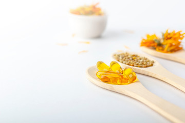 Herbal capsule, natural vitamins, dry calendula flowers at wooden spoon on white background. Concept of healthcare and alternative medicine: homeopathy and naturopathy. Close up, copy space for text