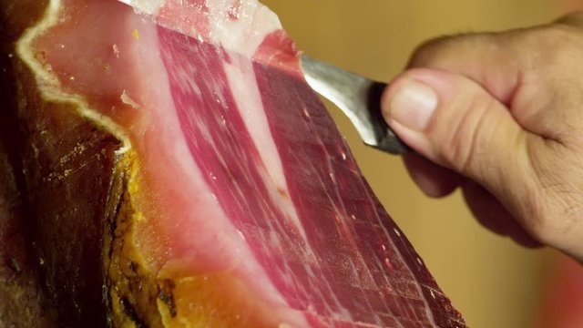 CU Male hand cutting thin slices off Pata Negra ham (jamon)
