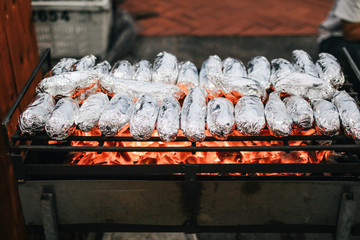 Baked sweet potatoes wrapped with aluminum foil roasting.Burned by heat on the fireplace, with...