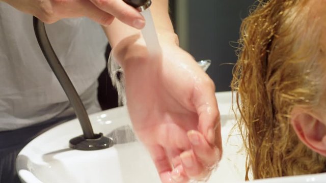 CU Female hairdresser testing water temperature before washing hair of client