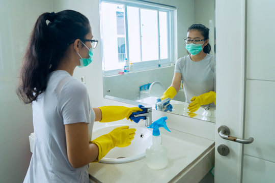 Asian woman using disinfectant to clean bathroom
