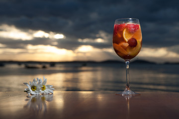 Refreshing fizzy drink on wooden table with white flower and sunset in the background