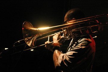 Black man playing shiny trumpet with black background
