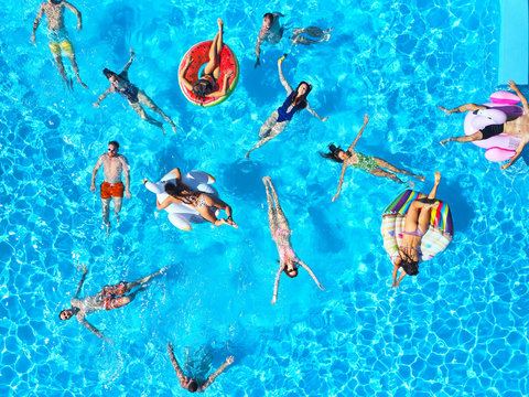 Aerial of friends having party in swimming pool with inflatable flamingo, swan, mattress. Happy young people relax at luxury resort on sunny day. View from above. Girls in bikini sunbathing in a sun.