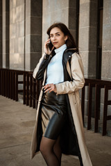 portrait Businesswoman girl in the city speaks by mobile phone. Wearing a black and white coat. Standing up