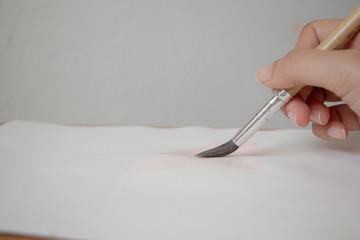 Hand holding paint brush on paper. Artist paints a picture.