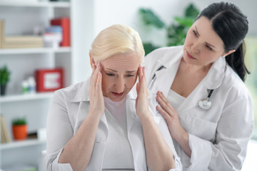 Obraz premium Blonde doctor holding her head and suffering from a headache, her colleague looking concerned
