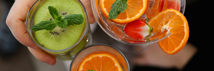 Top view of three different delicious cocktails with mint and juicy fruits. People holding cold fresh beverages in glasses. Festive celebration and holiday concept