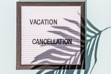 A message Board with the words " vacation cancellation" on a blue background. On the Board, the shadow of a palm leaf. Concept pandemic coronavirus and the global crisis