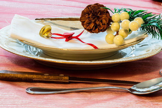 Preparations for the end of year dinner at home. Two porcelain plates with gold edges and a small bell and a pine cone used as decorations.