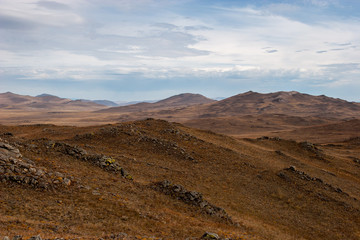Landscape in a hilly area. Evening brown colors. Clouds in the sky.