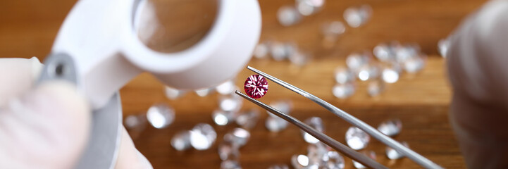 Close-up of jeweller hands in gloves looking at gemstones through magnifier. Professional goldsmith installing brilliant. Gold jewelry production concept