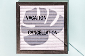 A message Board with the words "vacation cancellation" on a blue background. On the Board, the shadow of a monstera leaf. Concept pandemic coronavirus and the global crisis