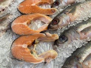 Close up of fresh raw fish in pieces of ice. Chilled fish lying on counter of supermarket with crushed transparent ice.