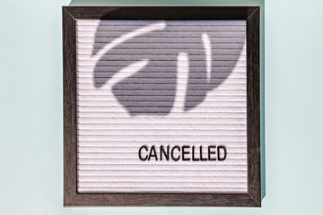A message Board with the words canceled on a blue background. On the Board, the shadow of a monstera leaf. Concept pandemic coronavirus and the global crisis